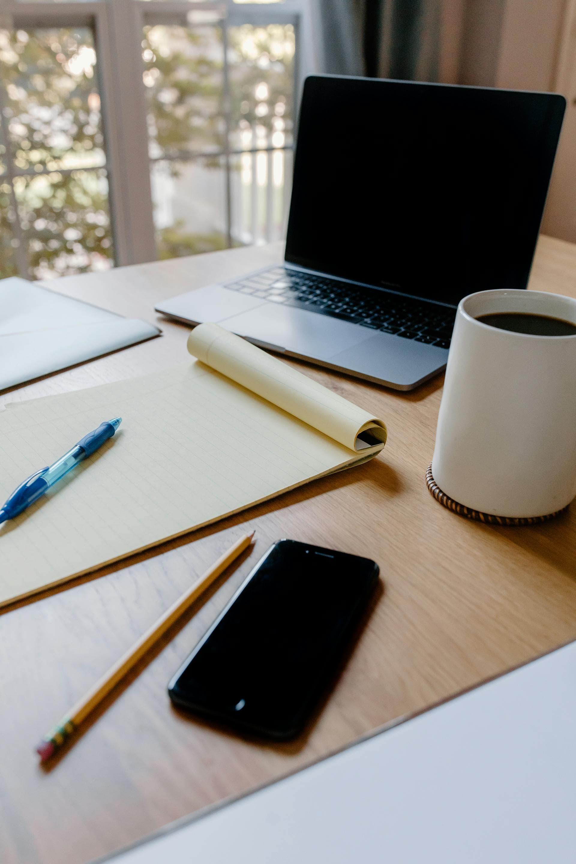A laptop, notebook, and coffee mug on a sunlit kitchen table — a quiet workspace for sorting through a separation
