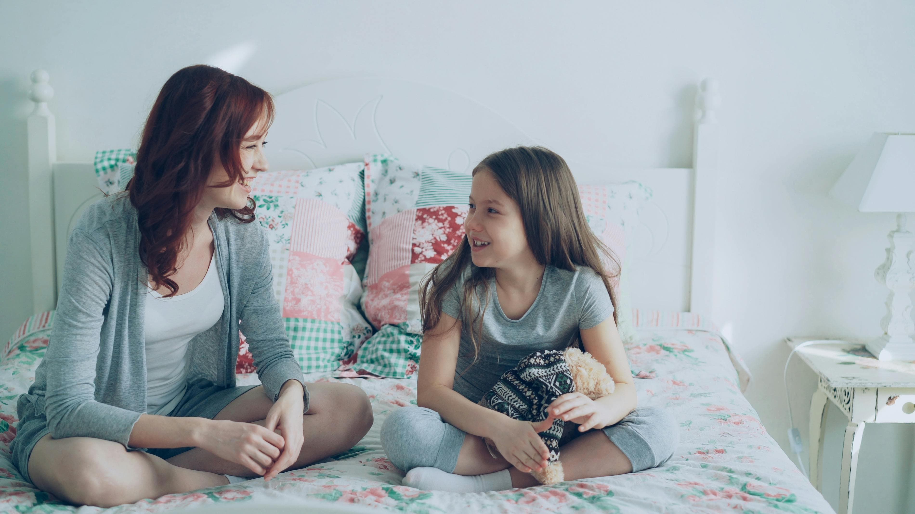 A mother and young daughter sitting on a bed smiling at each other — representing a BC family navigating child support arrangements